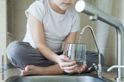 Child is using filter to purify drinking water. Kitchen faucet. Filling cup beverage. Pouring fresh drink. Healthy lifestyle. Quality check. World water monitoring day. Environmental pollution concept