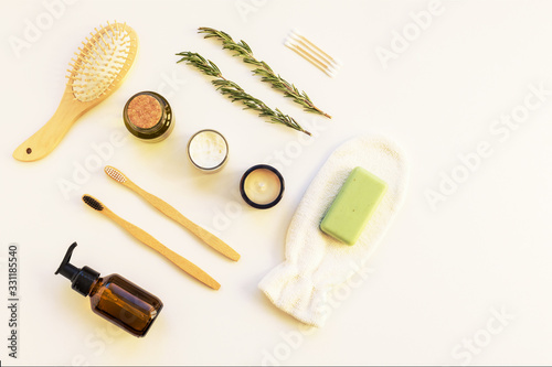 Natural cosmetics, soap, wooden toothbrushes, cosmetic mittens, comb and sprigs of rosemary on a white table.