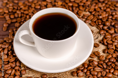 A cup of black aromatic coffee in a white cup on a background of roasted coffee beans arabica coffee on a wooden table