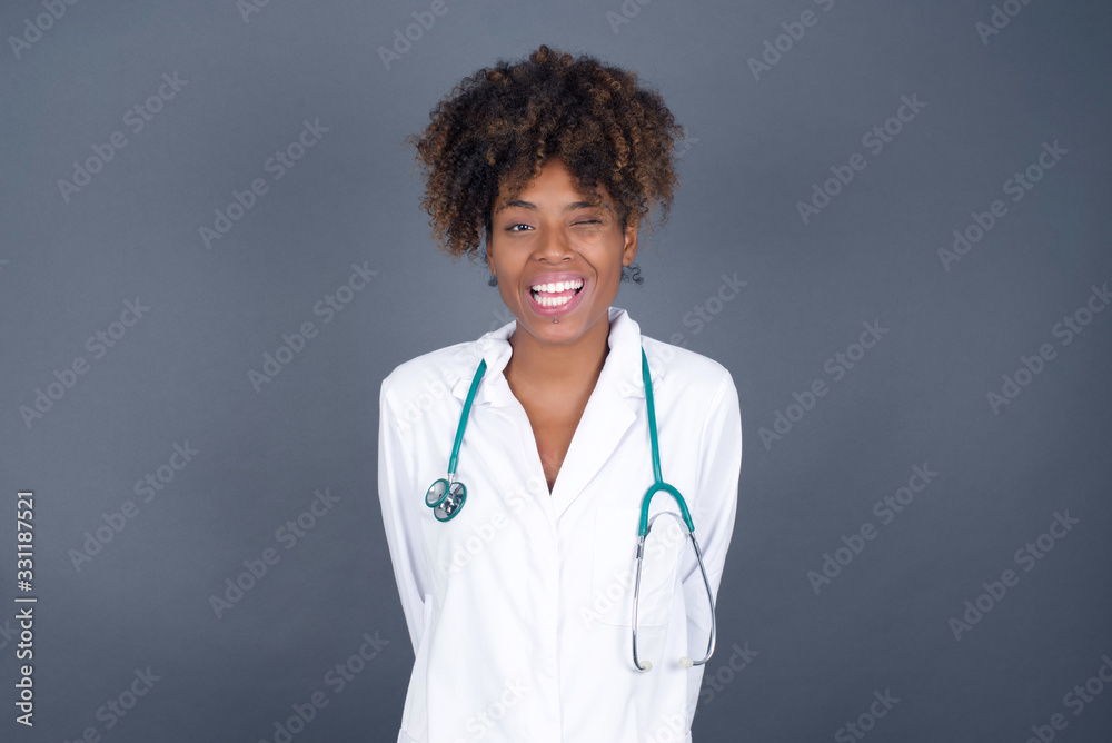 Cute young doctor female with long hair wearing medical uniform blinking her eyes with pleasure having happy expression. Facial expressions and people emotions concept. Cute young doctor female with long hair wearing medical uniform blinking her eyes with pleasure having happy expression. Facial expressions and people emotions concept.