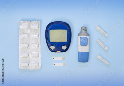 Diabetic kit: glucometer, test strips, lancet, metformin tablets. Top view, blue background, empty space.