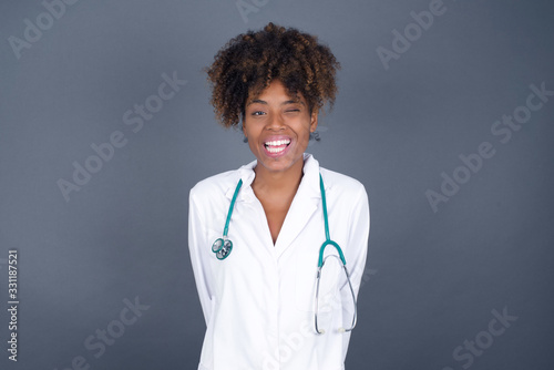 Cute young doctor female with long hair wearing medical uniform blinking her eyes with pleasure having happy expression. Facial expressions and people emotions concept.