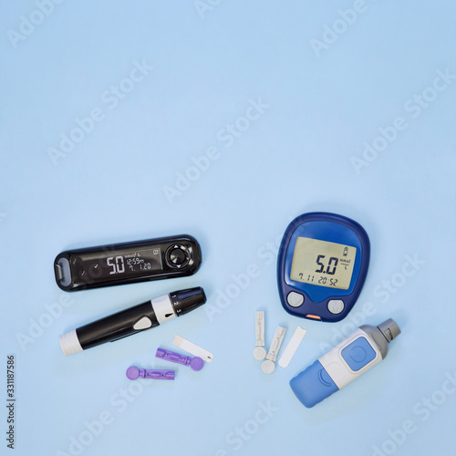 Diabetic kit: two types of glucometers, test strips, lancet. Top view, blue background, empty space.