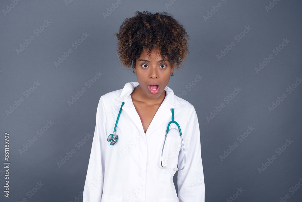 Expressive facial expressions. Shocked stupefied doctor woman wearing medical uniform, feels stunned from what she sees aside on blank gray Wall Expressive facial expressions. Shocked stupefied doctor woman wearing medical uniform, feels stunned from what she sees aside on blank gray Wall