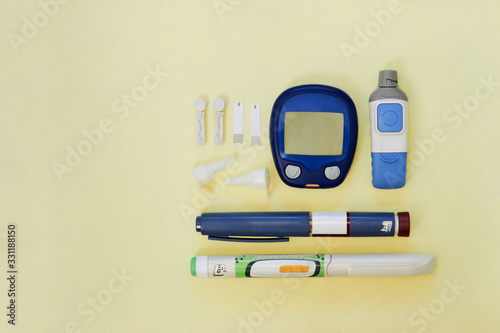 Diabetic kit: glucometer, test strips, lancet, insulin pens, metformin tablets. Top view, yellow background, empty space.