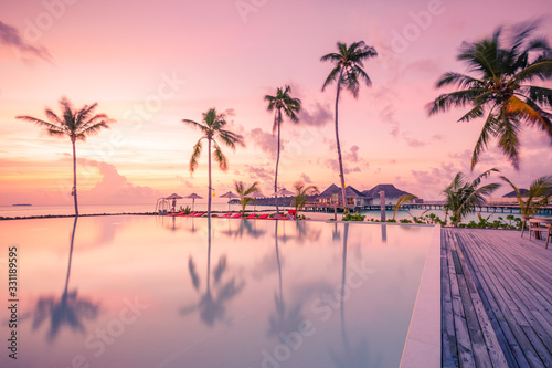 Fototapeta Naklejka Na Ścianę i Meble -  Luxury sunset over infinity pool in a summer beachfront hotel resort at tropical landscape. Tranquil beach holiday vacation background mood. Amazing island sunset beach view, palms swimming pool