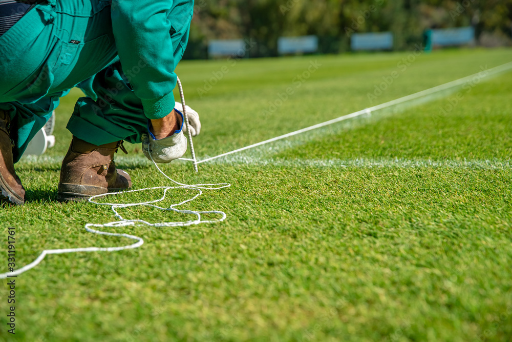 Stretching a rope for lining a football field using white paint on the grass - obrazy, fototapety, plakaty 
