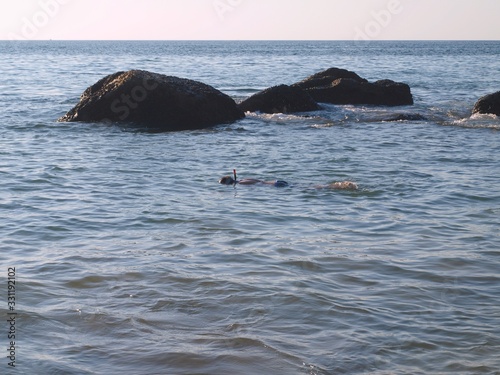Snorkeler swimming near stones in the water. Boy swims in the sea with diving mask and breath snorkel and observes a seabed