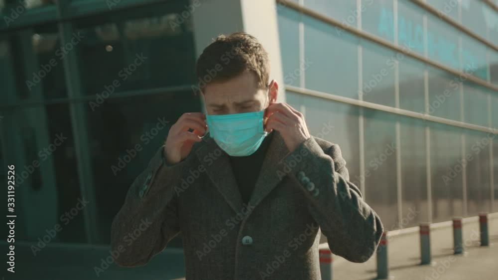 Close up man removes Protective Face Mask sneeze coughs hold suitcase COVID-19 coronavirus infection near airport pandemic disease virus male tourist epidemic air health illness slow motion