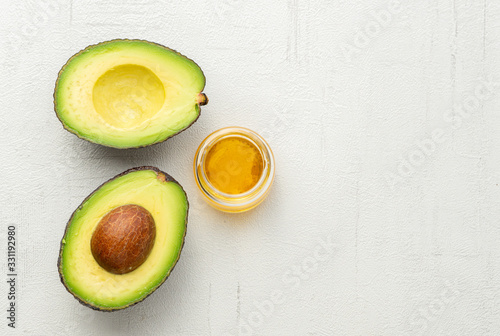 Avocado oil. Cosmetic. Transparent bottle. Half of avocado. Close up. Grey background. Top view. 