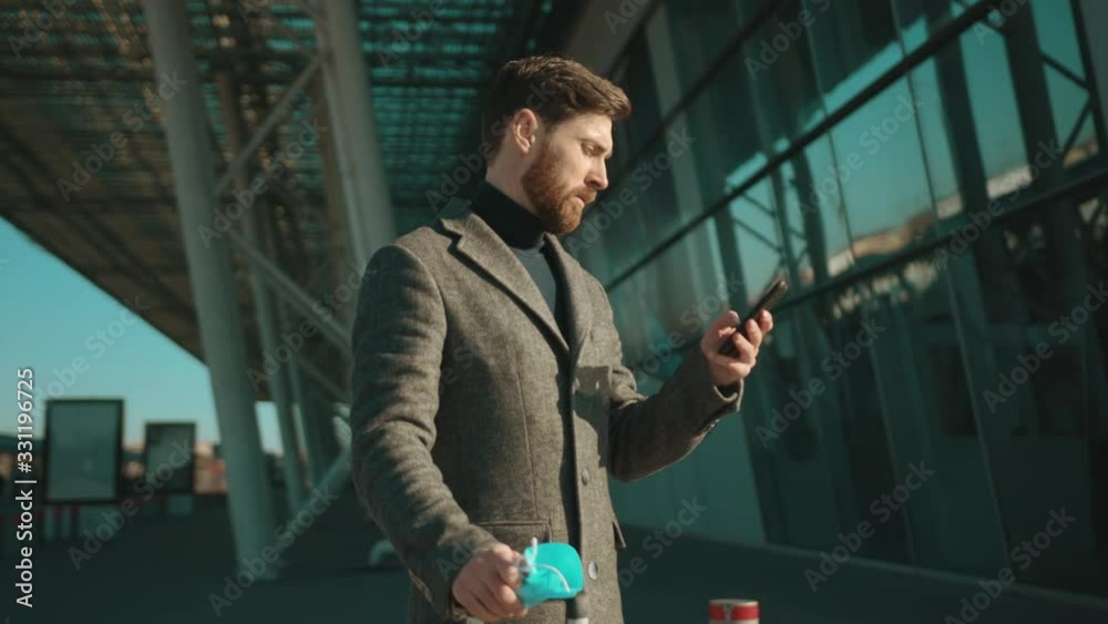 At sunlight man removes Protective Face Mask sneeze coughs use phone COVID-19 coronavirus infection near airport pandemic disease virus male tourist epidemic air health illness slow motion