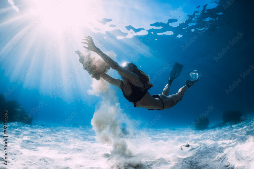 Woman free diver glides with white sand over sandy sea. Freediving underwater in Hawaii