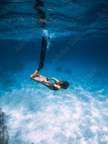 Woman freediver glides with fins over sandy sea bottom. Freediving and sun light in ocean