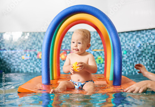 Cute little boy wearing a diaper holding his rubber toy, sitting on a floating colorful construction in the swimming pool. Concept of healthy childhood © anatoliy_gleb