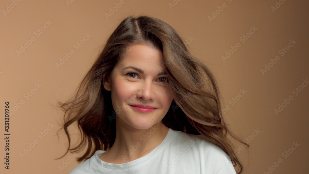 Fototapeta premium Monochrome natural makeup look Caucasian woman in studio in white t-shirtwith healthy shiny hair blowing Happy smiling brunette with blowing hair