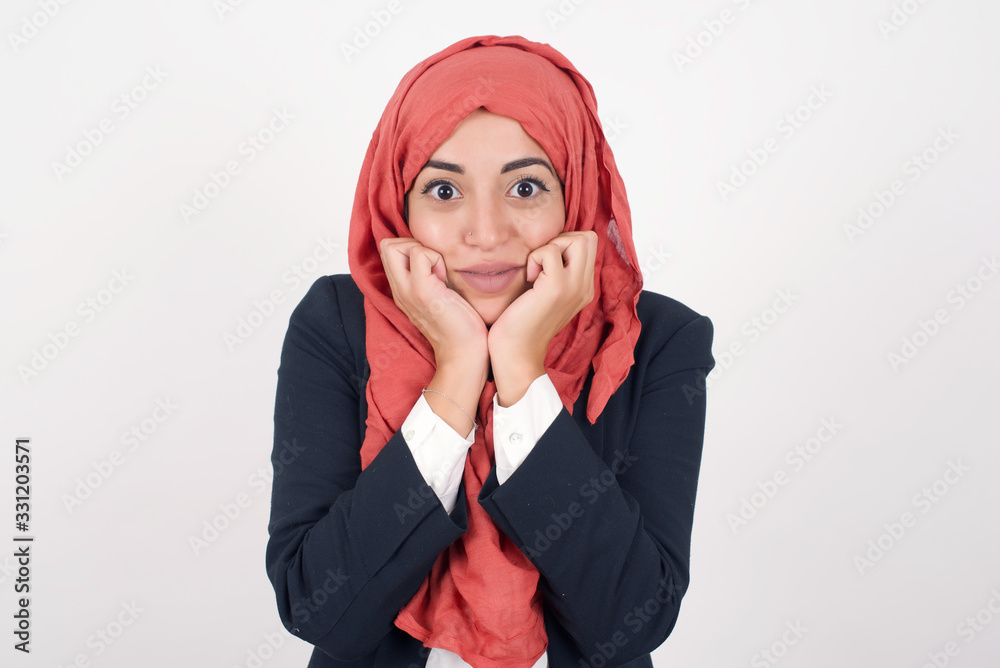 Dreamy young European woman keeps hands pressed together under chin, looks with happy expression, has toothy smile, isolated over gray background Dreamy young European woman keeps hands pressed together under chin, looks with happy expression, has toothy smile, isolated over gray background