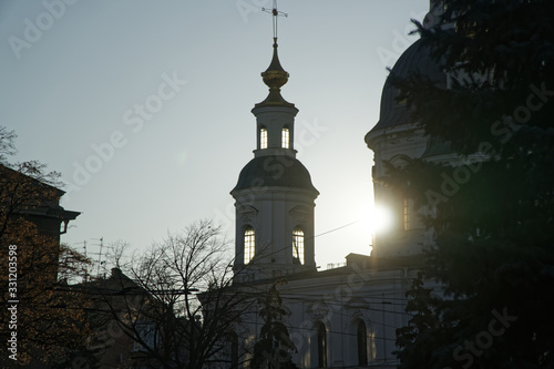 Part of ortodox church in front view with sun behind the clounds. The sun rays breaks through the dome of the church. Cross of church against blue sky. photo