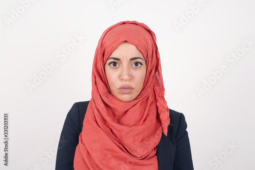 Portrait of outraged young woman with oval face, blue eyes and long hair wearing White  sweater frowning her eyebrows being displeased with something. Scowling pretty female isolated over grey.ï¿½