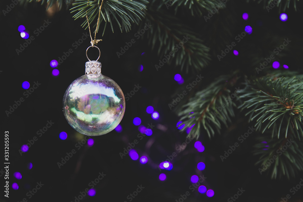 Fototapeta premium Horizontal background. Live spruce decorated for Christmas with transparent gold and purple garland with bulbs. Copy space.