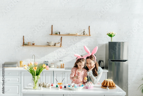 Photography happy kid and mother with bunny ears near chicken eggs, decorative rabbits, east