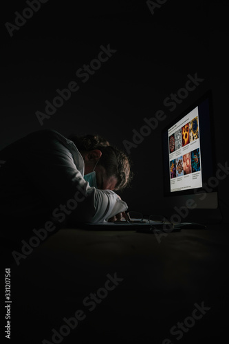 Stock photo of a mangled doctor sleeping at his desk in front of the computer. He wears a white coat and a mask.