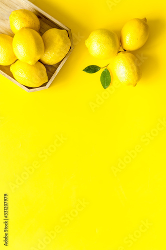 Ripe lemons in tray on yellow backgroud top-down frame copy space