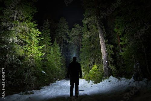 Figure on forest path at night with headlamp illuminating the trees and path photo