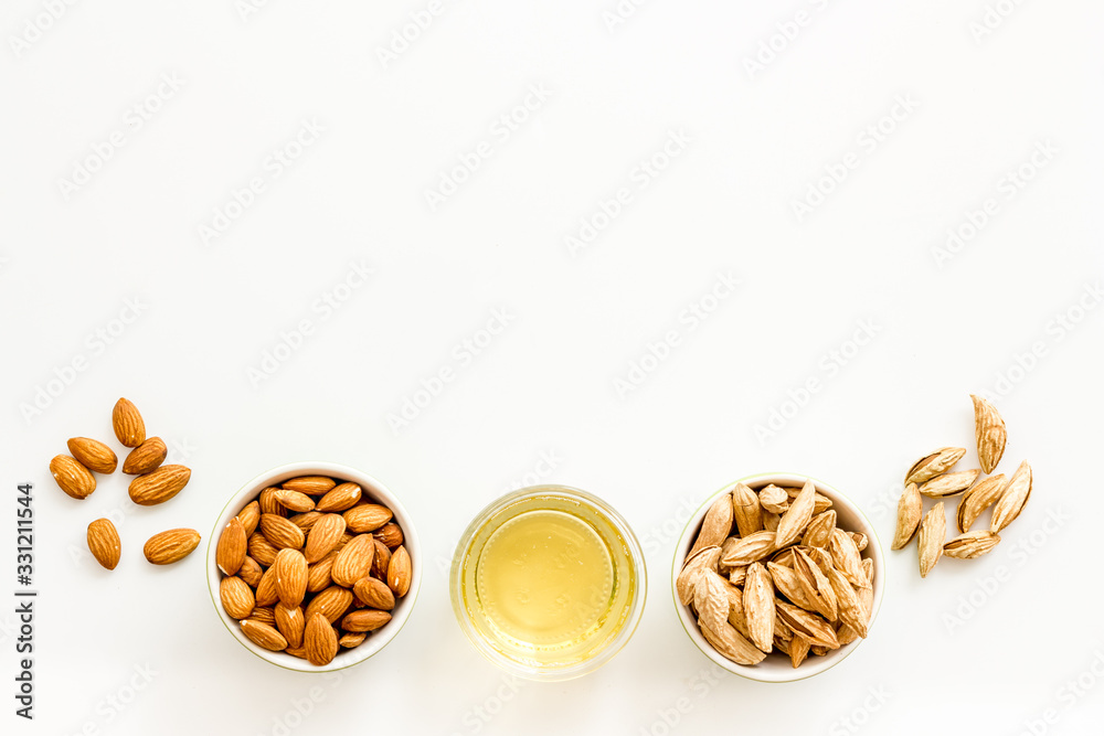 Almond oil - for cooking - in glass bowl near nuts on white background top-down copy space Almond oil - for cooking - in glass bowl near nuts on white background top-down copy space