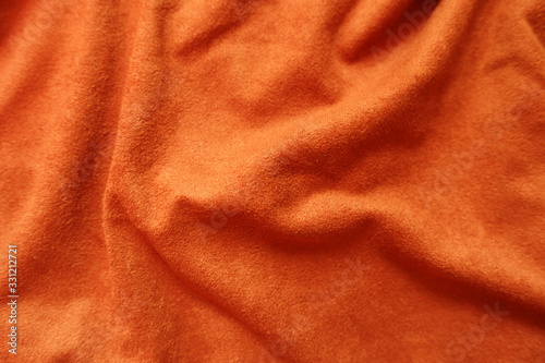Surface of bright reddish orange artificial suede fabric in soft folds