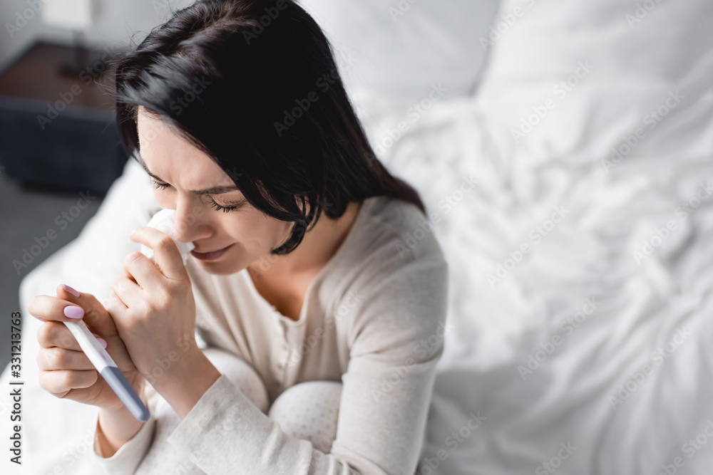 overhead view of upset woman crying and holding pregnancy test overhead view of upset woman crying and holding pregnancy test