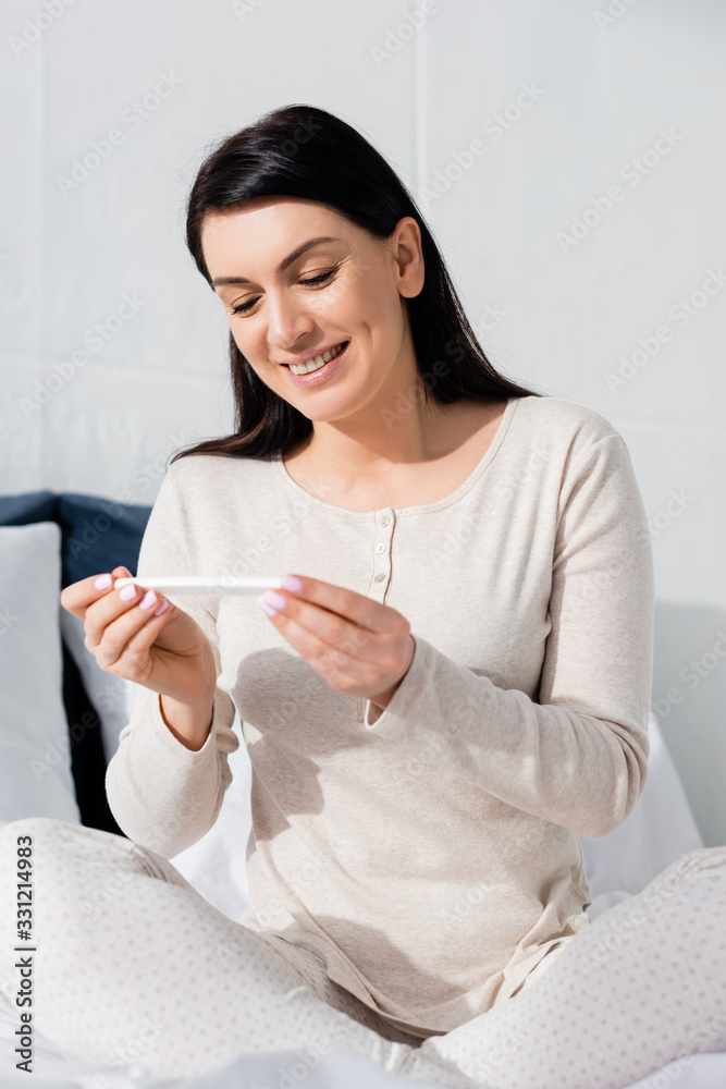 happy pregnant woman looking at pregnancy test in bedroom happy pregnant woman looking at pregnancy test in bedroom