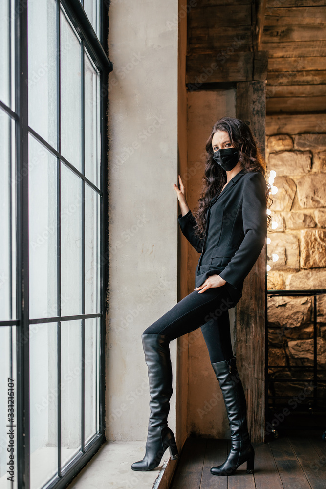 A woman in a medical mask looks out the window. A woman in a medical mask looks out the window.