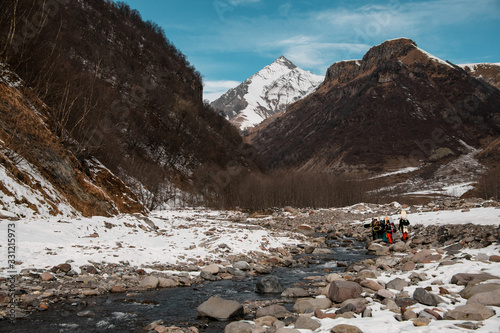 group of traveling people with ski equipment walks along mountain river.