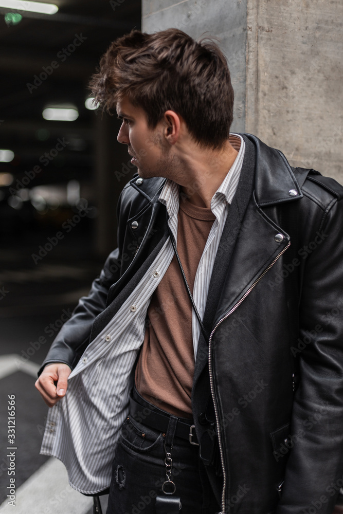 Fashionable modern young hipster man with a stylish hairstyle in trendy  oversized leather jacket in a