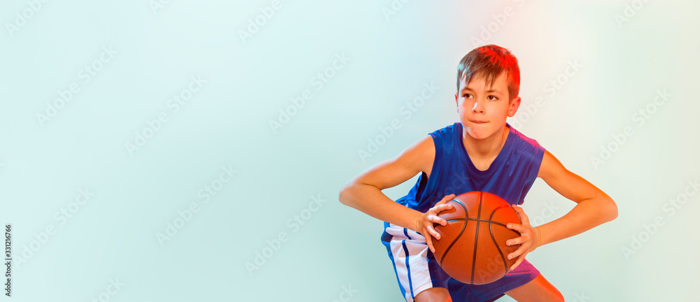 Kid playing basketball isolated on blue background in mixed light