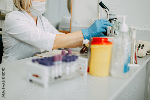 Blood test process in laboratory. Doctor hands making blood test. Many blood test-tubes with blood on the table. Covid-19 testing.