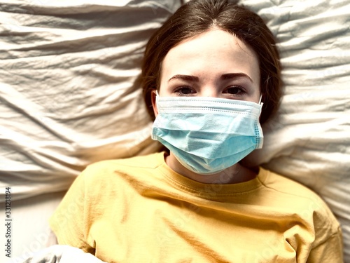 a teenage girl in a medical mask in bed during corona virus quarantine time lack of freedom