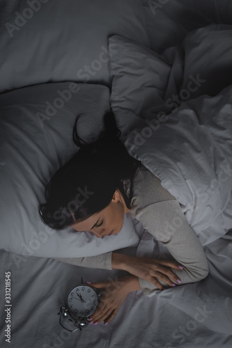 top view of woman with sleep disorder looking at alarm clock in bedroom