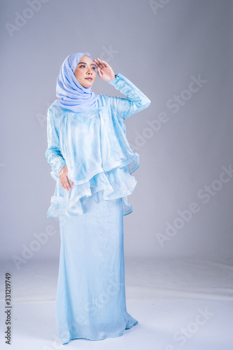 Full length portrait of a beautiful female model wearing traditional dress and hijab, a lifestyle apparel for Muslim women on grey background. Idul Fitri and hijab fashion concept.