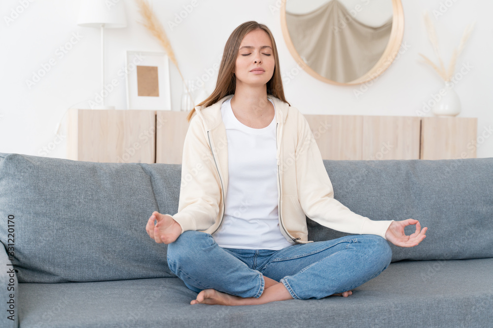 Mindful healthy young woman sitting on couch in lotus pose, practicing ...