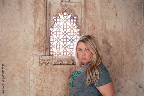 Cute blond woman tourist (30s) gives a fierce look by an oranate window near in a city palace in Udaipur India photo