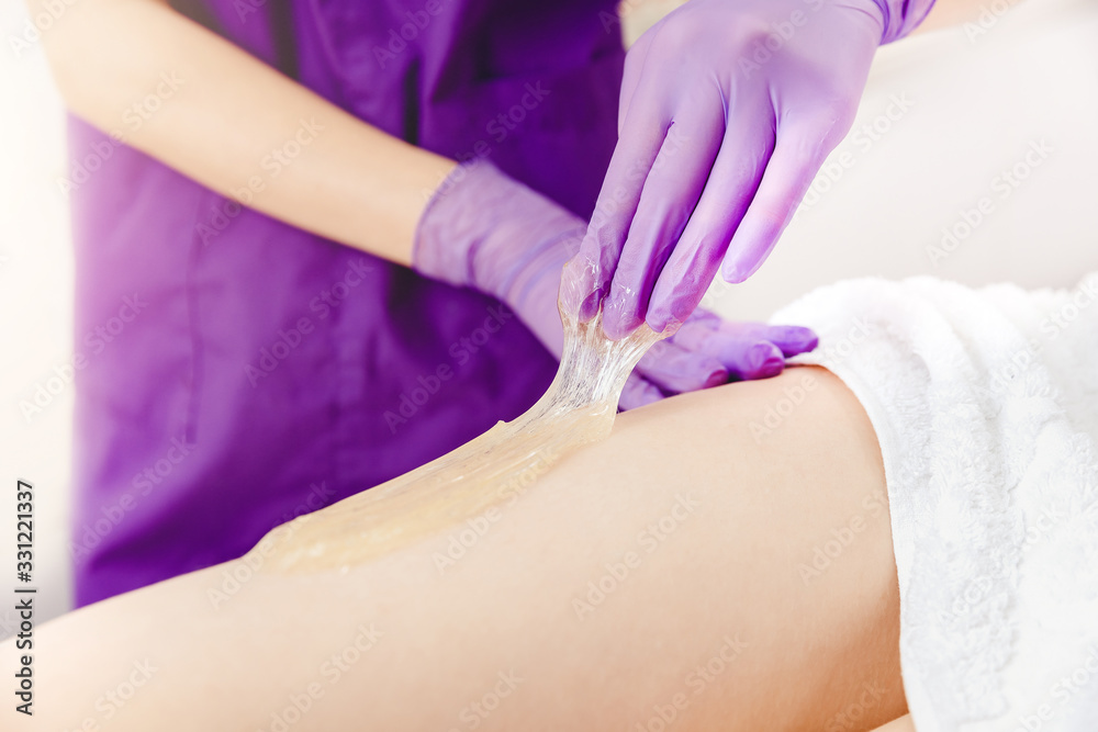 Fototapeta premium Depilating legs young woman with liquid sugar pasta in spa salon