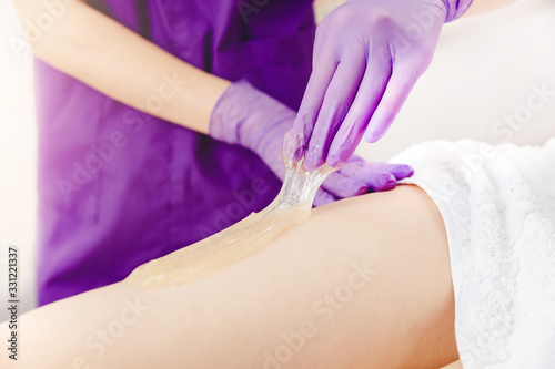 Depilating legs young woman with liquid sugar pasta in spa salon photo