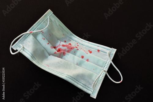 blood from cough patient on hygienic mask for protection nose and mouth in black fabric background
