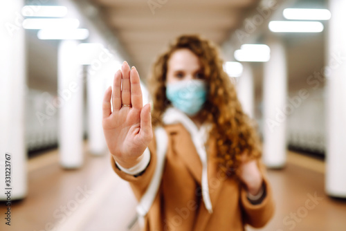 Hand stop sign. Woman in a sterile medical mask on her face, shows stop hands gesture for stop coronavirus outbreak at subway station. The concept of preventing the spread of the epidemic.