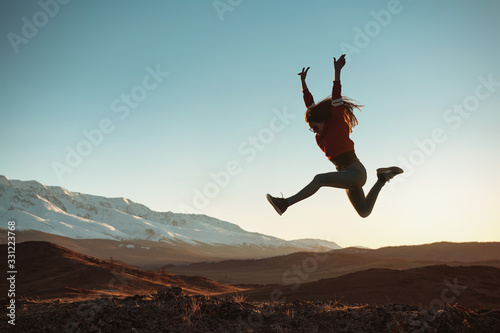 Photographie Happy girl jumps against mountains at sunset