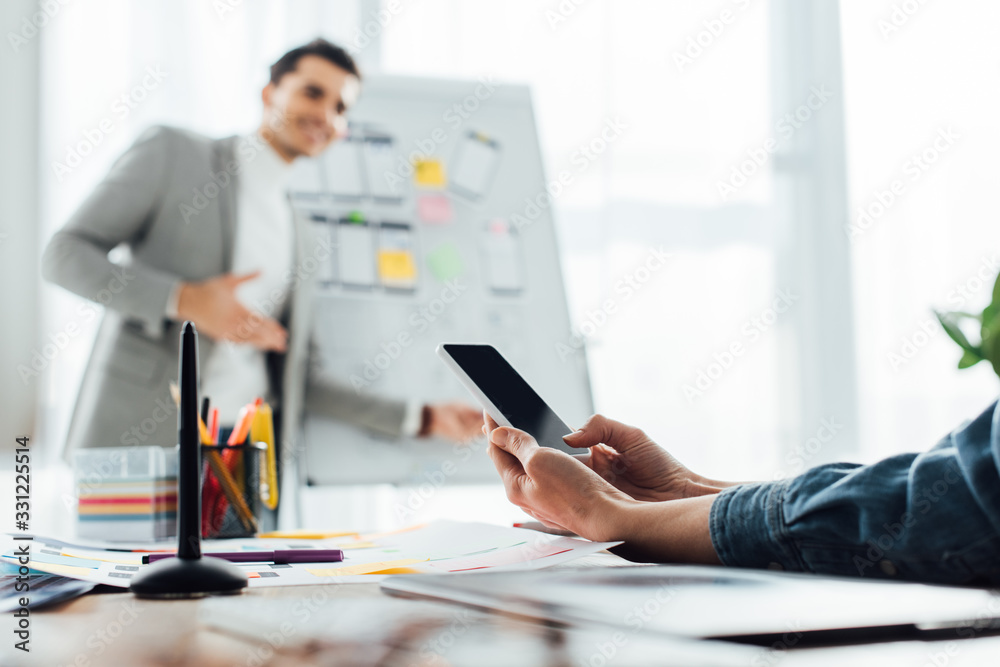 Selective focus of ux designer looking at colleague near whiteboard with layouts in office Selective focus of ux designer looking at colleague near whiteboard with layouts in office