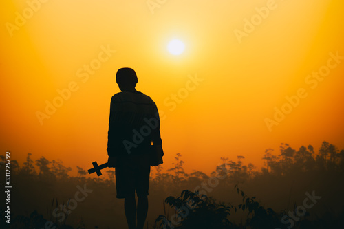 human holding cross on the mountaind at sunset background. christian silhouette concept. photo