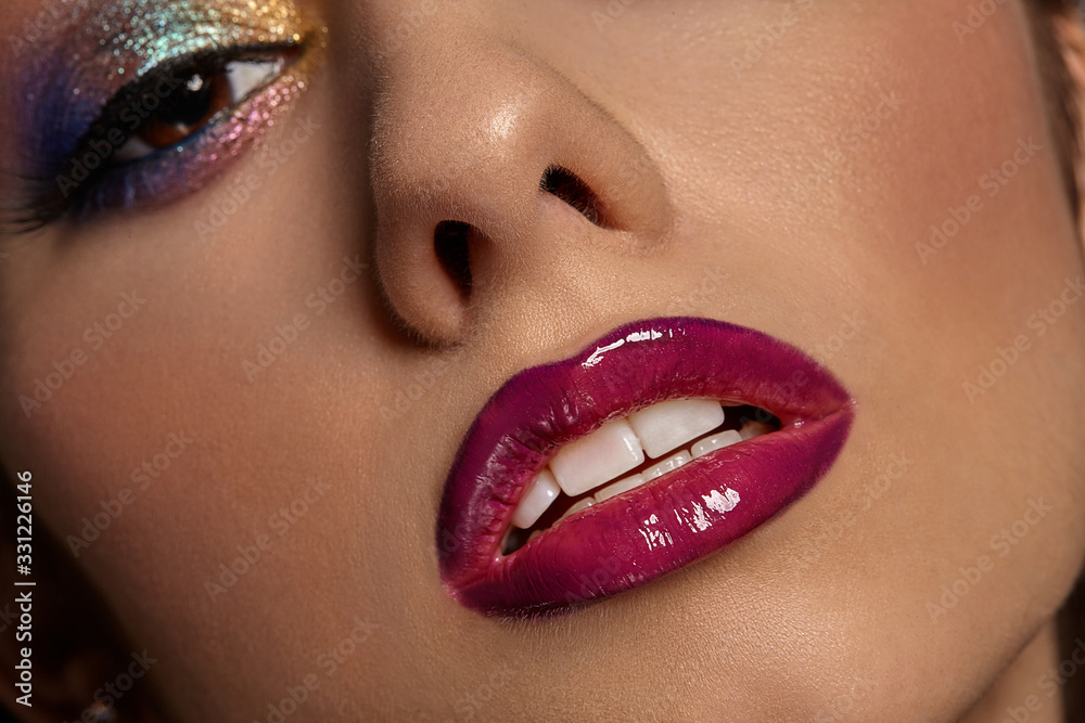 Naklejka premium Face of a lady with luxury makeup and perfect skin. Blue and golden eyeshadow, long eyelashes, glossy burgundy lips and white teeth. Close up
