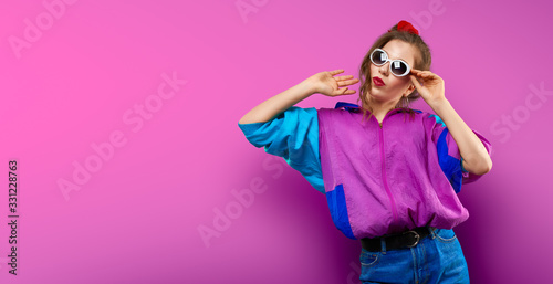 Cool teenager. Fashionable DJ girl in colorful trendy jacket and vintage retro sunglasses enjoys style of 80s � 90s vibes. Teenager Girl at disco party. Young fashion model on pink color background. © LoopAll